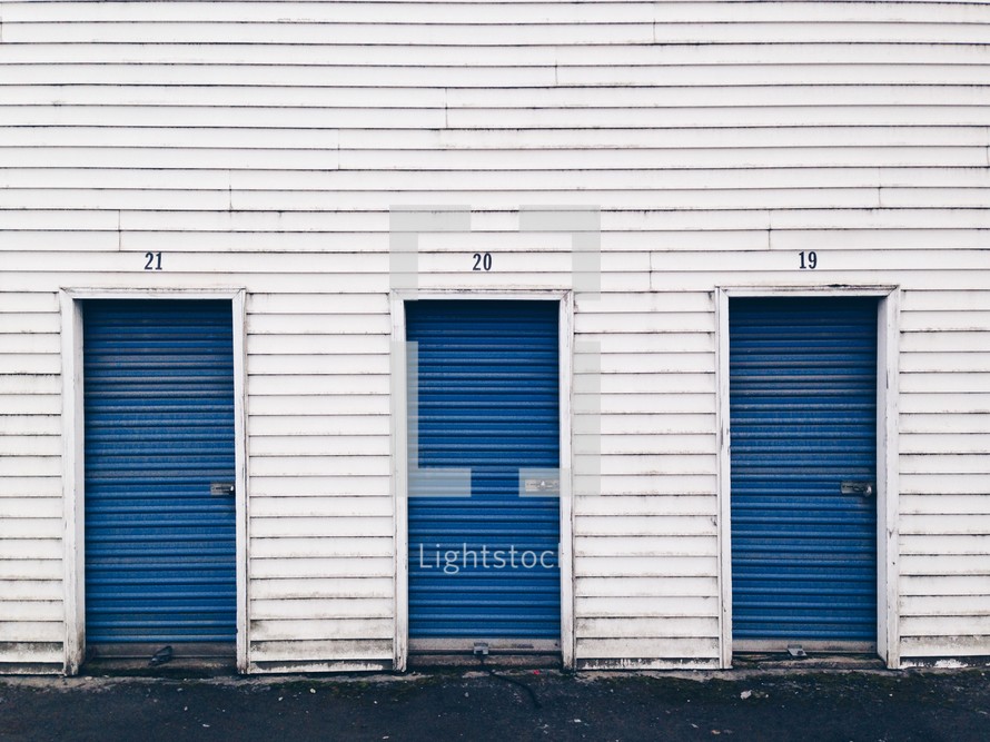 Three blue doors in a row on a white frame building.