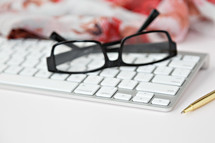 reading glasses on a computer keyboard, pen, and scarf 