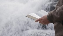 a man standing in front of a waterfall reading a Bible in Asheville, NC
