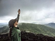 woman with raised hand standing on a mountaintop 