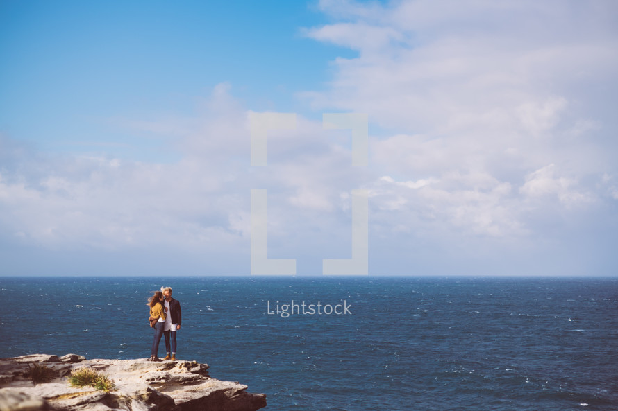 couple standing on the edge of a cliff near the sea 