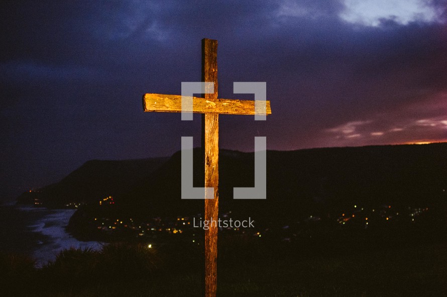 Wooden cross on a hill over a city at nightfall.