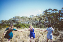 Three girls holding hands running in a field