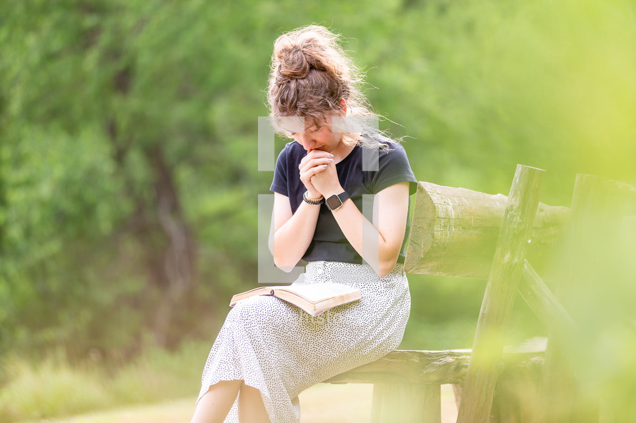 Young woman sitting on a bench praying with Bible in lap