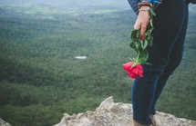 woman holding a rose standing at the edge of a cliff 
