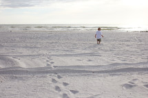 Toddler boy walking on a white sandy beach
