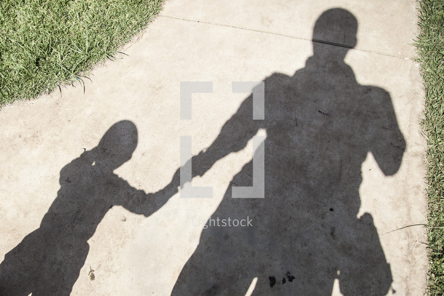 Shadow of man holding his son's hand on a sidewalk.
