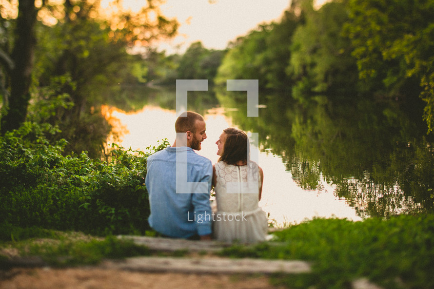 A happy couple relaxes by a river bed at dusk.
