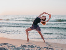 Portrait of young woman with long hair practicing classic exercises with emotions.Dancing ballerina in black silk dress on embankment near ocean or sea at sunrise or sunset
