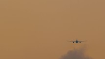 The airplane gains altitude and disappears into the yellow sunset sky