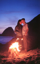 couple standing by a camp fire on a beach 