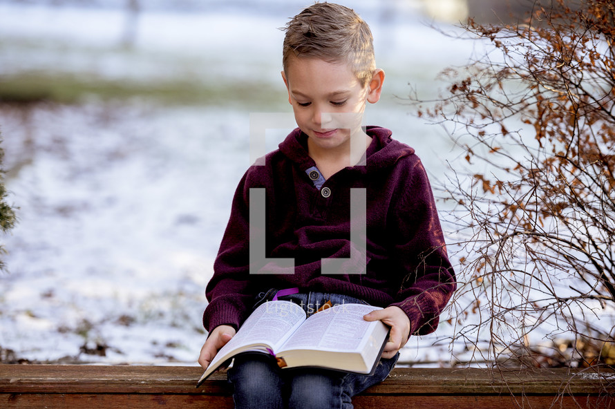 boy in a coat reading a Bible outdoors 