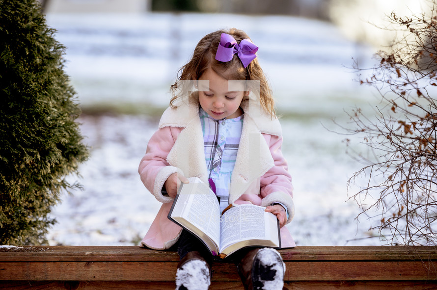girl in a pink coat reading a Bible outdoors 