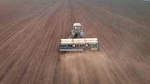 Drone sliding shot of a farmer in tractor seeding on sunny day, footage of sowing agricultural crops at field. Aerial view of a farmer in tractor seeding and cultivating land.