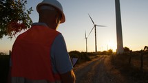 Silhouette of Engineer working against wind power plant generator at sunset