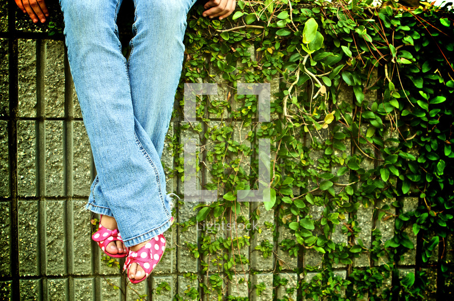 Woman sitting on ivy covered wall