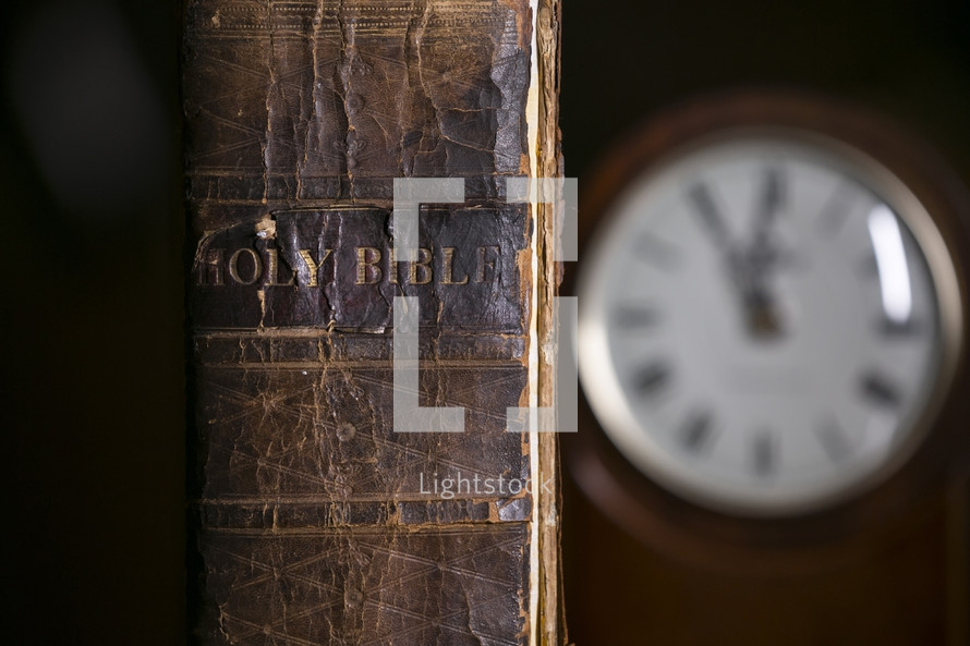 spine of an old leather Bible and clock on a desk 