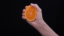 Woman squeezing an orange half on black background.