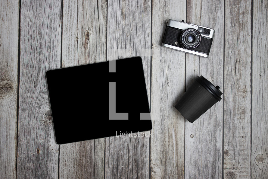 Camera, tablet, and cup on wooden background