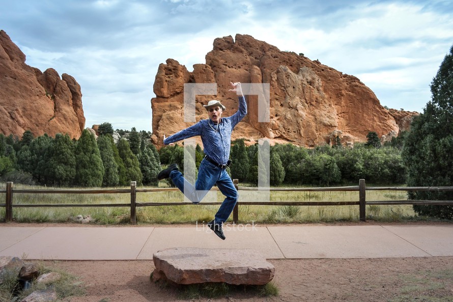 man jumping up in front of red rocks 