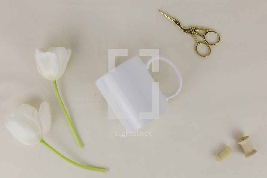 mug, spool, scissors, and white tulips on a white background 