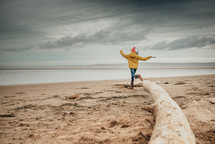 girl running on a beach in rain boots and a coat 