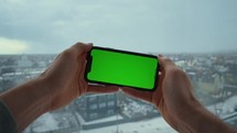 man holding smartphone with green screen playing online game device moves from side to side on the background winter city view
