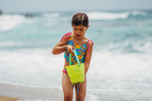 A young girl playing on the beach with a bucket.