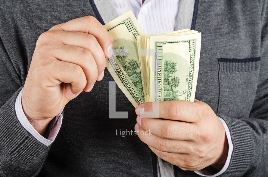 Man's hands holding a stack of hundred dollar bills.