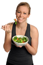 A smiling woman eating a bowl of salad.