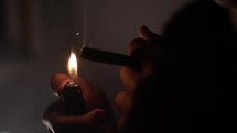 Troubled young man, teenage boy smoking drugs or cigarette, getting high, in dark, smoky room in cinematic slow motion lighting a joint.
