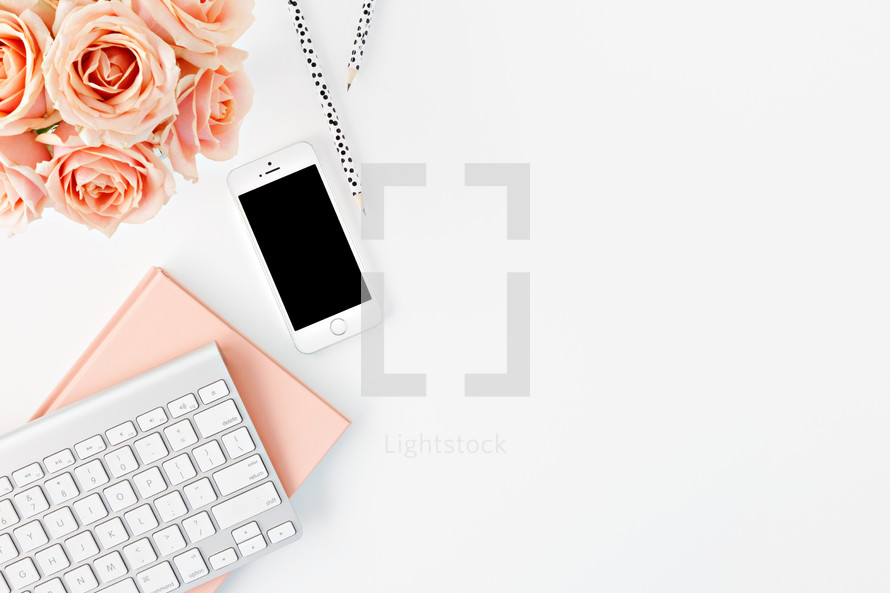 cellphone, computer keyboard, pencils, tea cup, and peach roses on a desk 