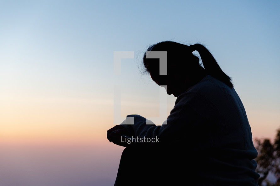 Silhouette of woman praying during sunset