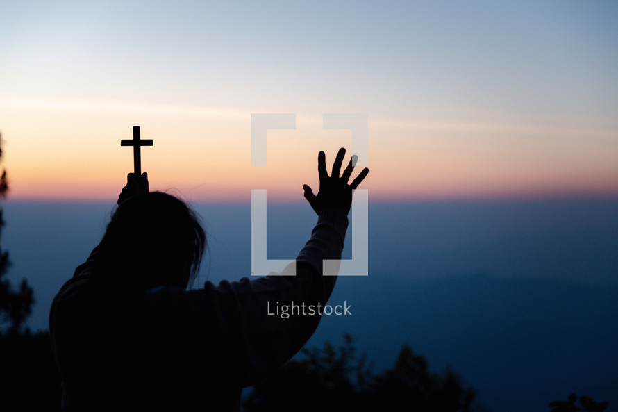 Silhouette of woman with cross praying during sunset