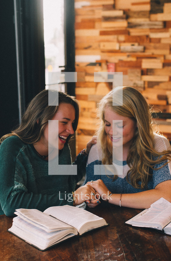 women praying over Bibles at a Bible study in a coffee shop 