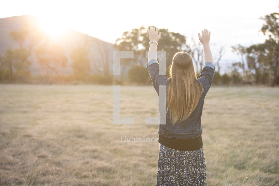 a woman standing in a field with raised hands 