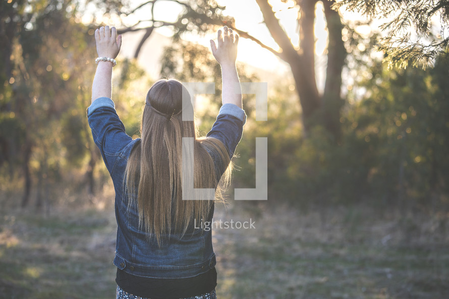 a woman standing in a field with raised hands 