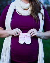 a pregnant woman in a knitted scarf holding baby booties 