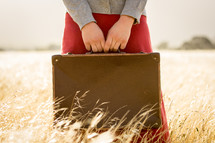 Girl holding suitcase in Brown Grass