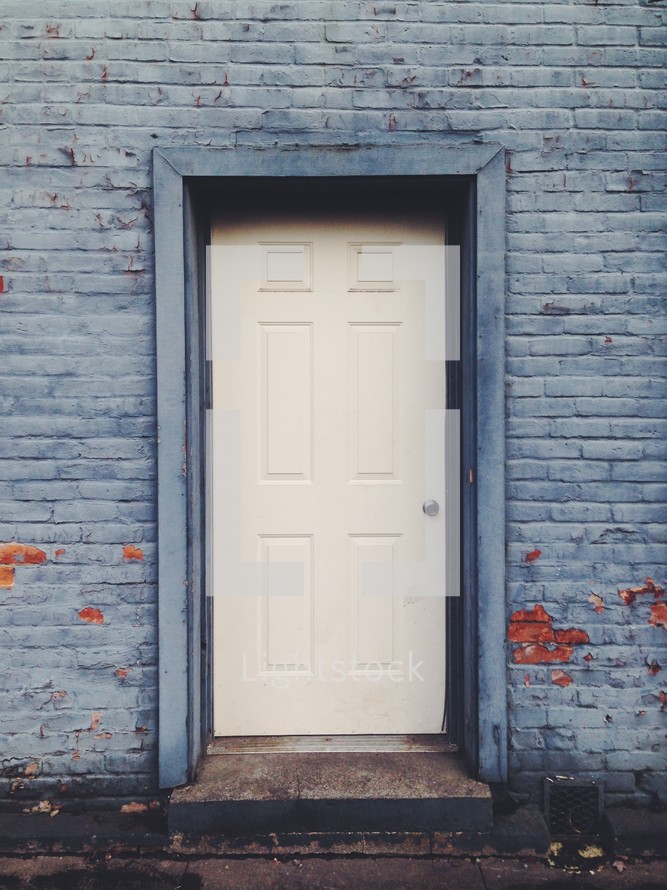 A white door in the side of a blue brick building.