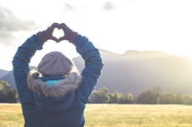 a woman standing outdoors in winter making a heart with her hands 