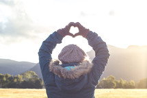a woman standing outdoors in winter making a heart shape with her hands 