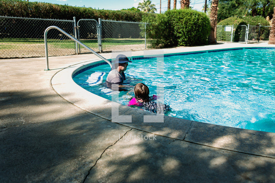 a father and daughter swimming in a pool 
