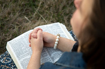 praying hands over a Bible outdoors 