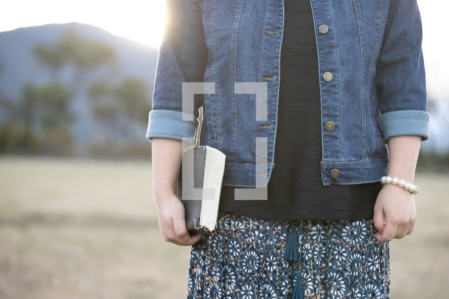 a woman standing in a field holding a Bible 