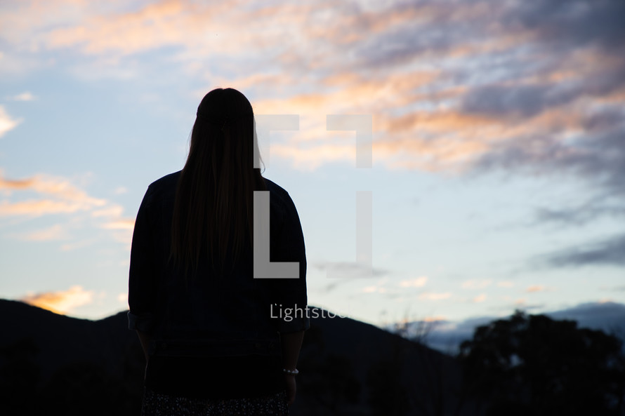 silhouette of a young woman standing outdoors at sunset 