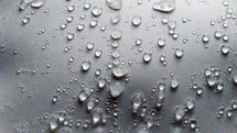 Small and large beads of water droplets and condensation begin to appear on a flat surface when cold weather and warm air mix and ice begins to melt forming condensation and life from water. 
