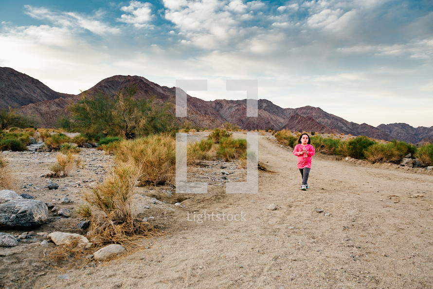 a girl child walking on a dirt road in a desert 