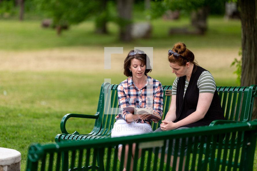 Two women doing a Bible study on a park bench