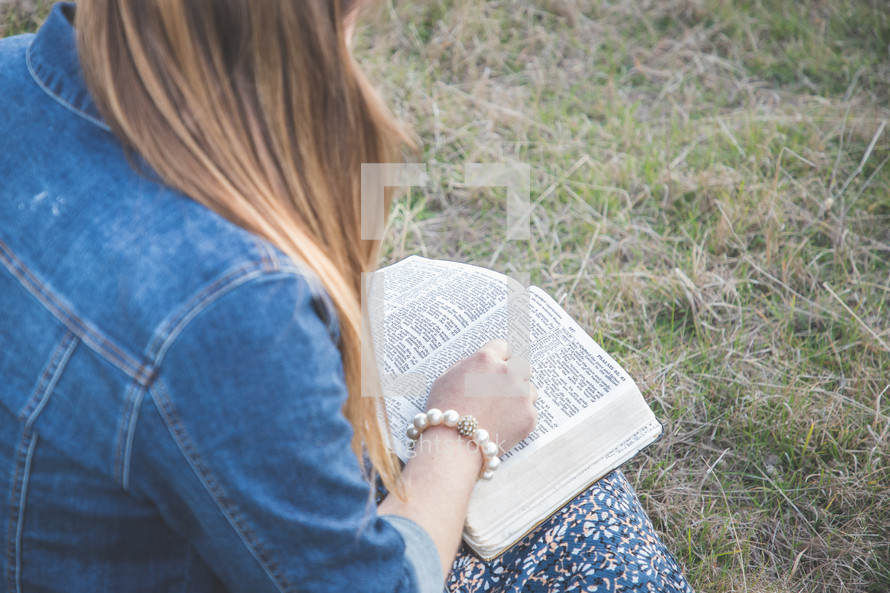 a woman sitting in grass reading a Bible 